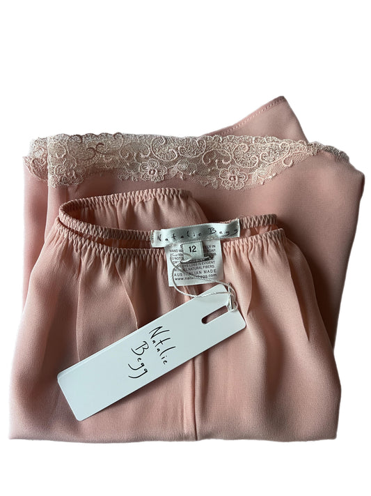 Folded pink satin garment with lace trim and a visible tag on a white background