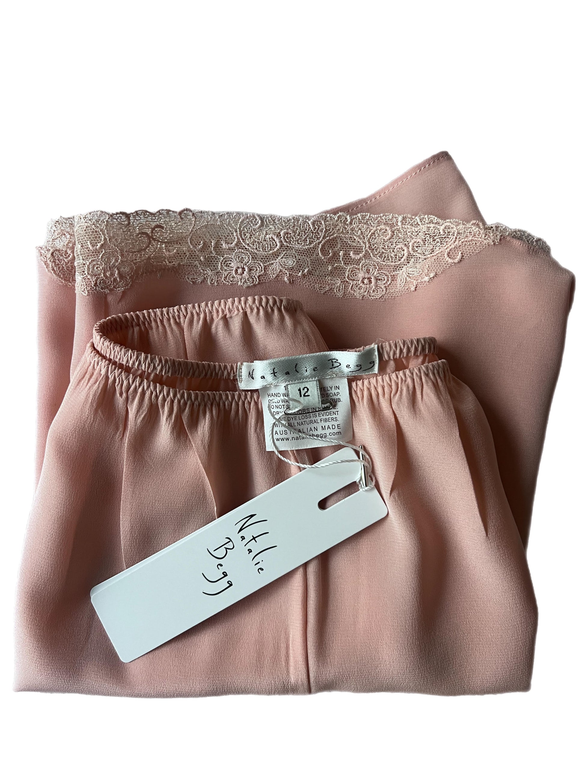 Folded pink satin garment with lace trim and a visible tag on a white background